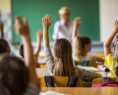 Children at school desks raising hands